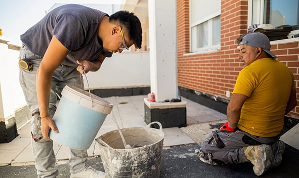 Latino construction workers laying tile, man pouring water into cement mix bucket