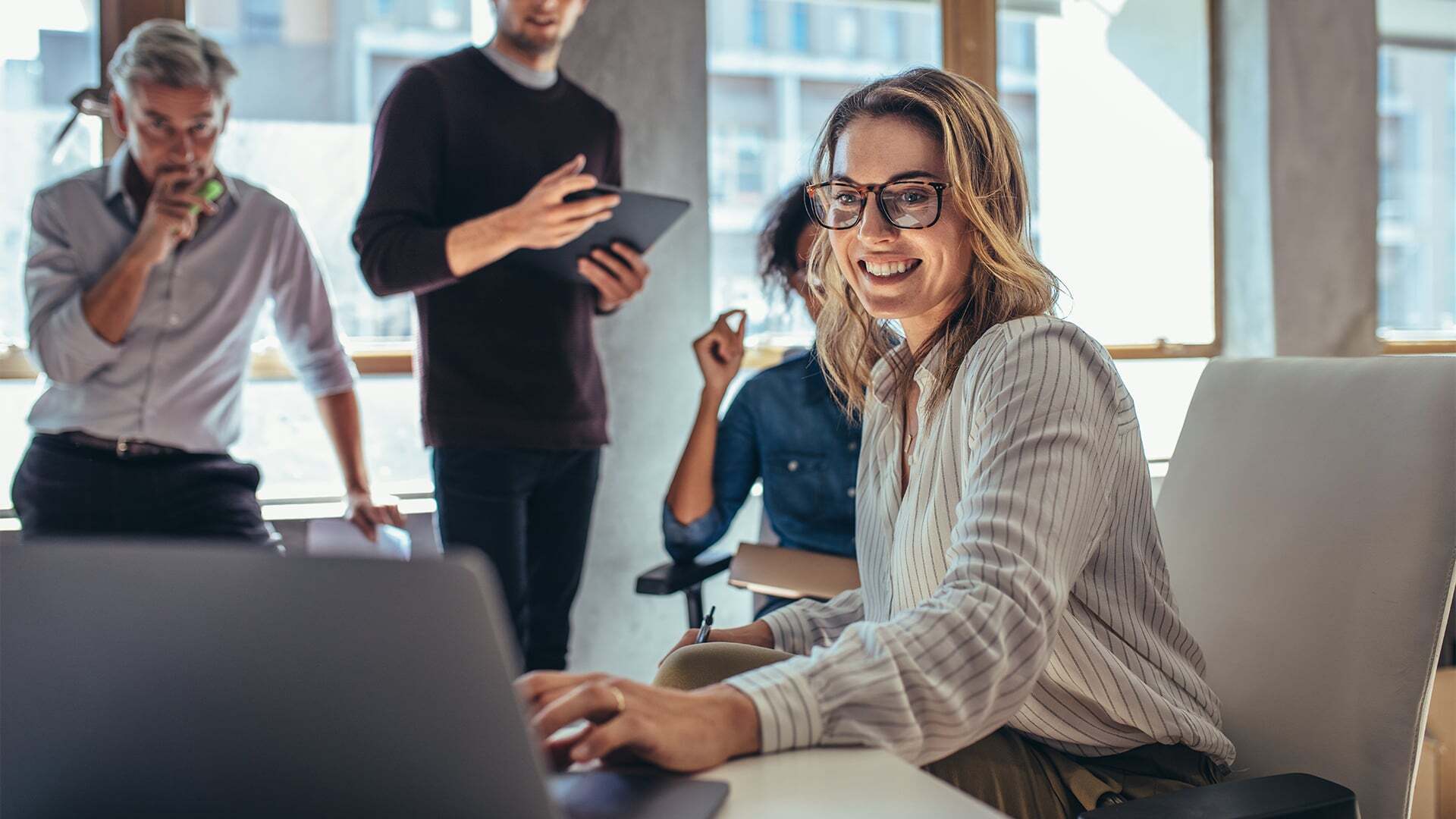 Digital marketing leader on laptop with a group of colleagues behind her providing input